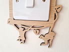 A wooden light switch cover with a carved design depicting two monkey figures.