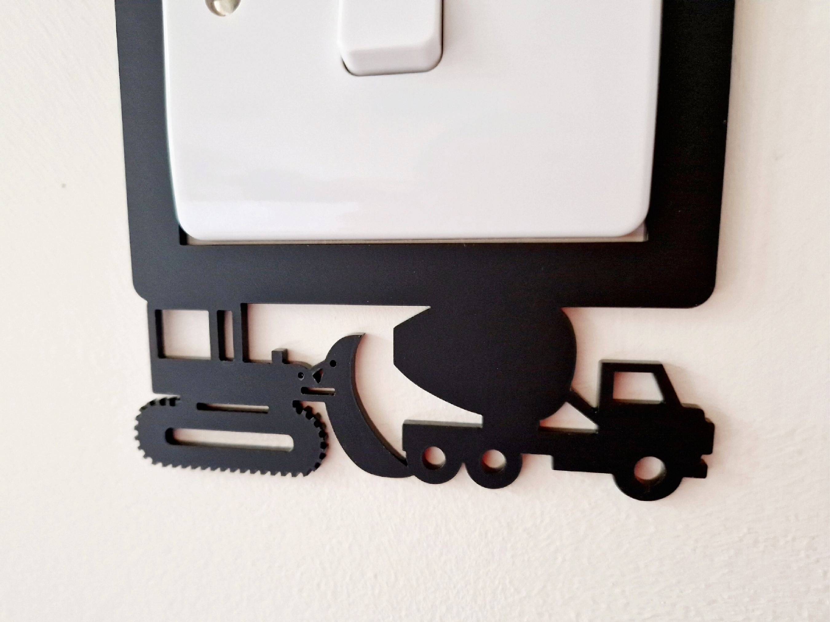 A wall-mounted light switch with a black construction vehicle cutout on the lower left side.