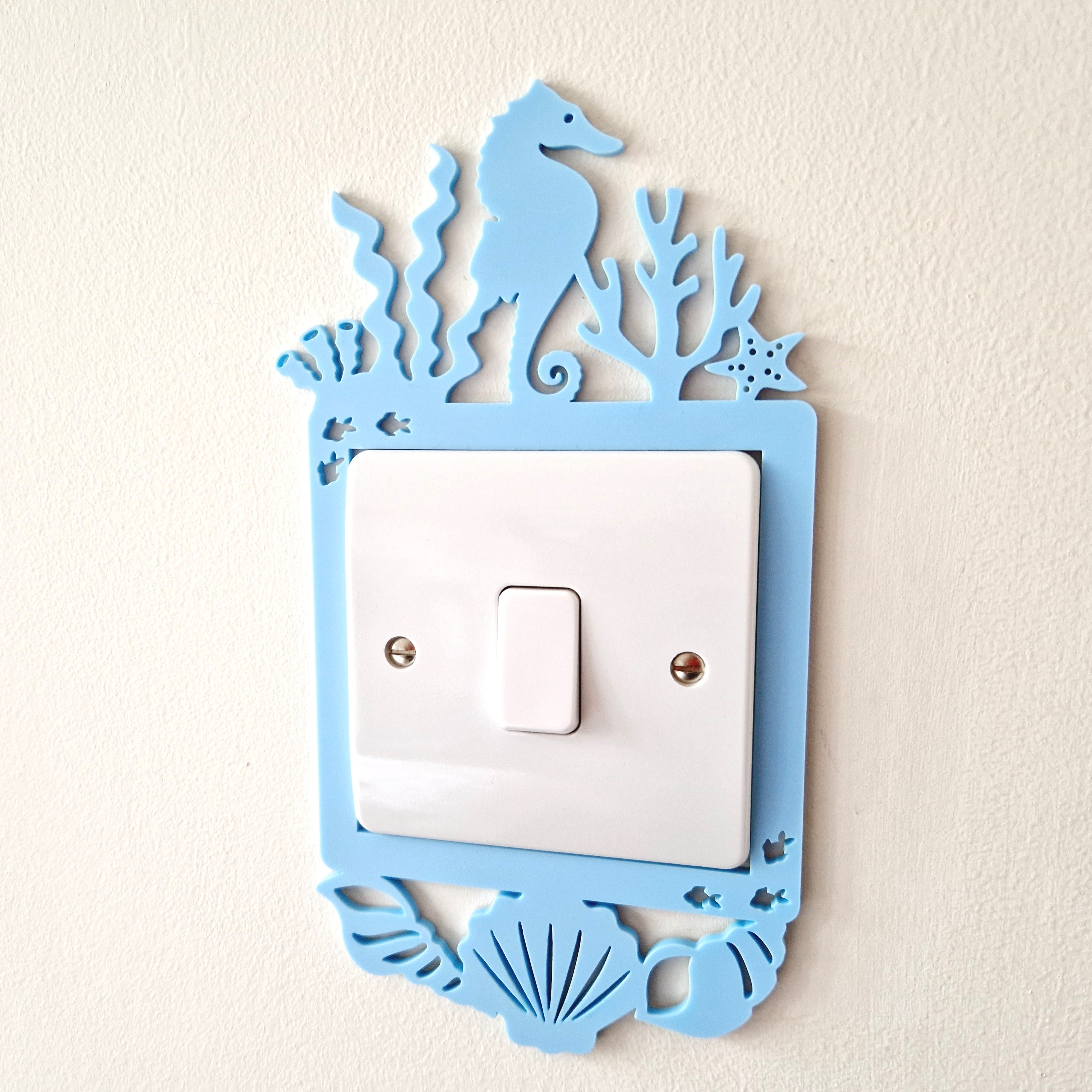 A light switch with a decorative blue frame featuring a seahorse and marine life.