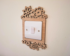 A wooden light switch with a floral design on the top and bottom edges, mounted on a wall.