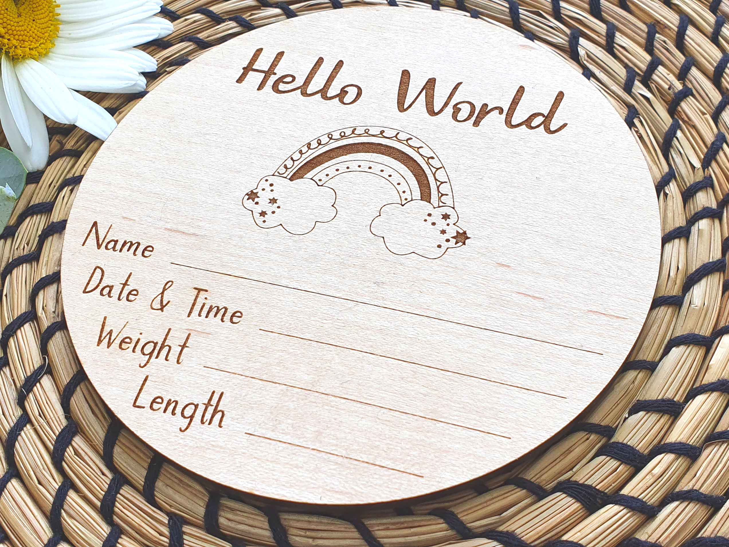 A wooden sign with the text "Hello World" and a rainbow graphic, placed on a woven placemat with a white daisy flower.