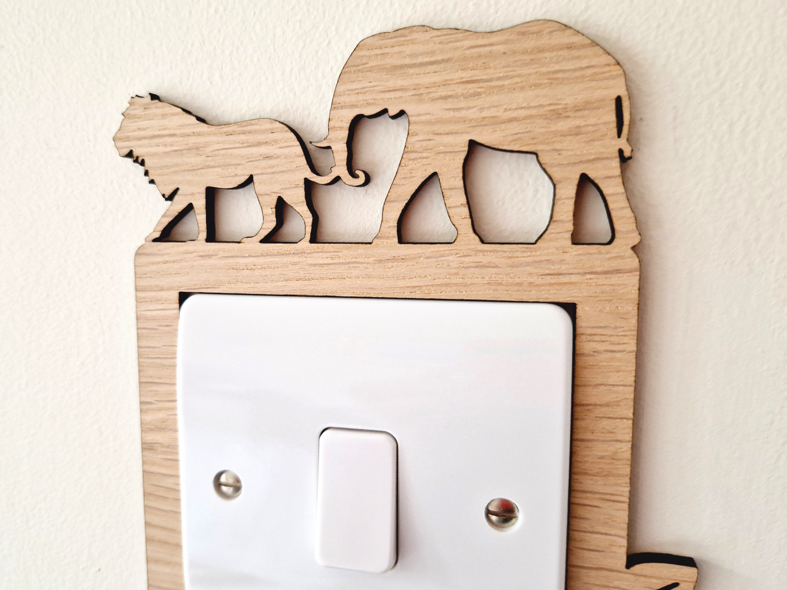 A wooden light switch with a silhouette of an elephant and a lion on it.