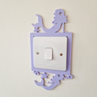 A purple mermaid-shaped light switch is mounted on a white wall.