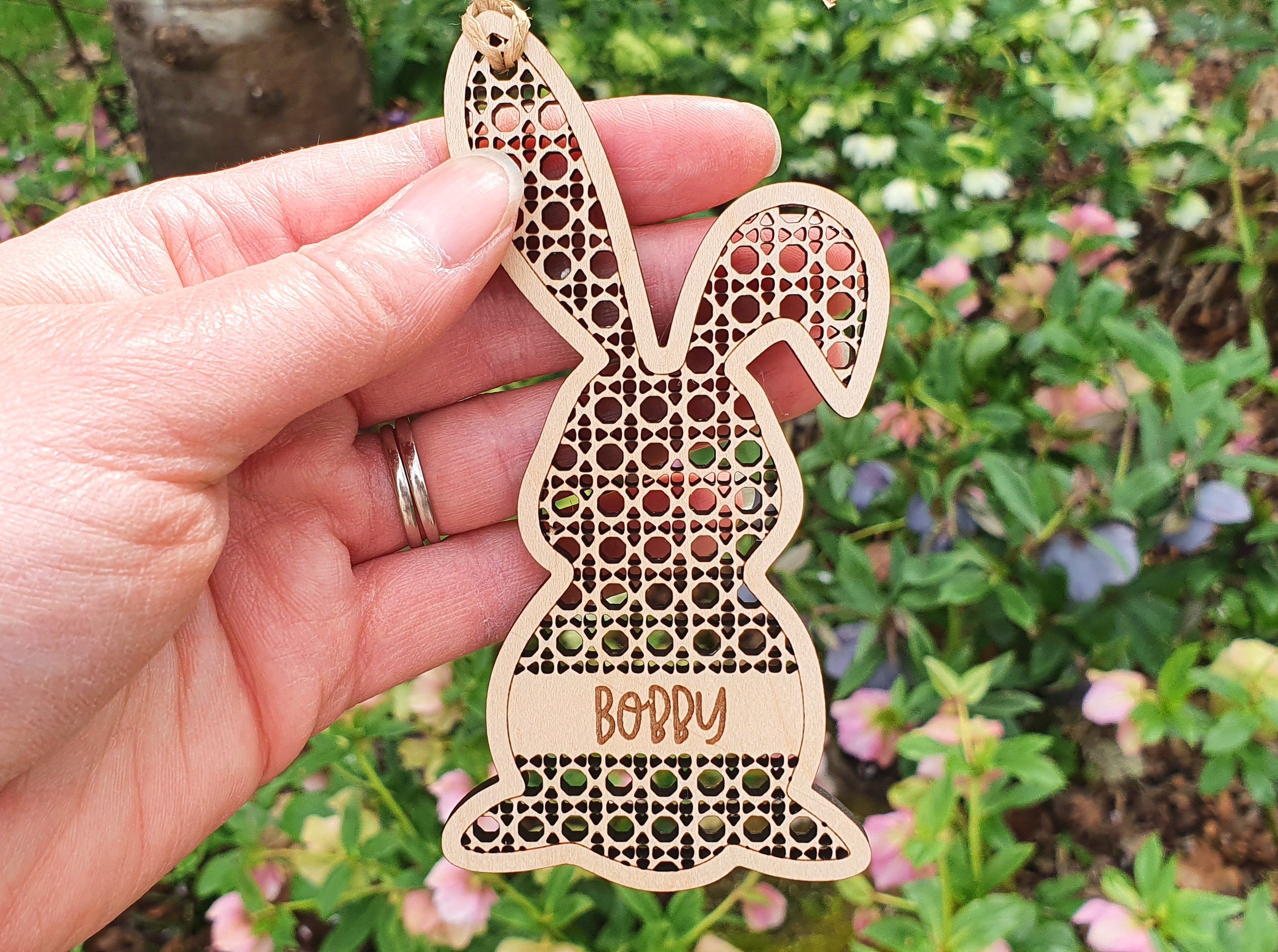 A hand holding a wooden Easter bunny ornament with the name "Bobby" engraved on it.