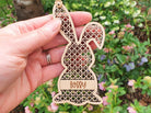 A hand holding a wooden Easter bunny ornament with the name "Bobby" engraved on it.