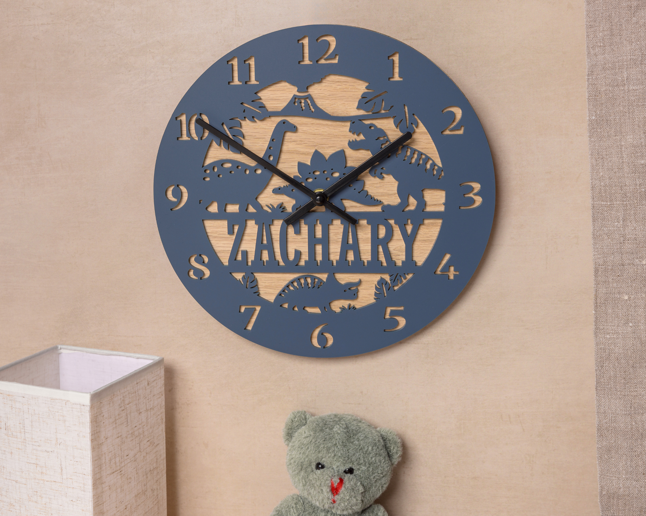 A wall clock with the name "ZACHARY" carved into it, along with a teddy bear and a lamp in the background.