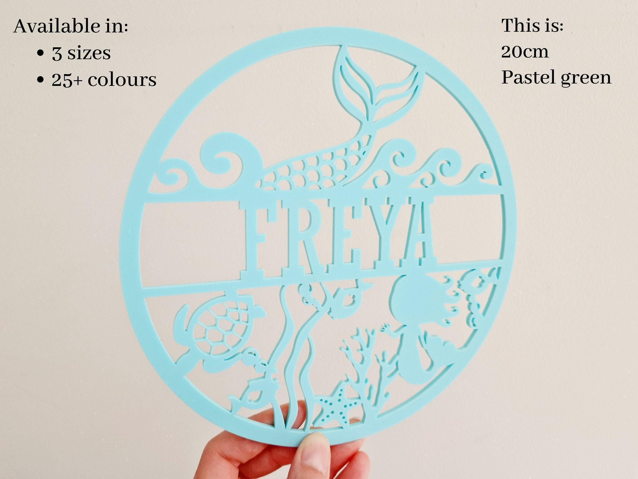A hand holding a light blue circular cutout with the name "FREYA" written on it.