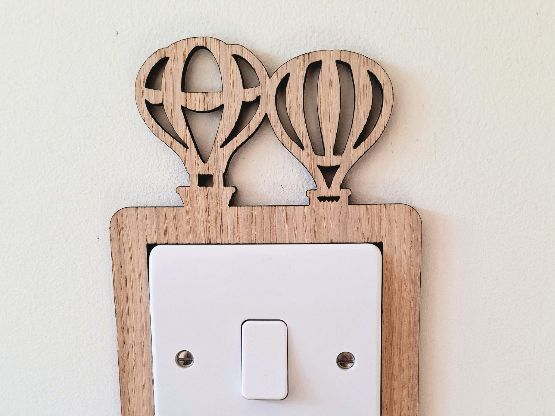A wooden light switch with two hot air balloon-shaped cutouts on top.