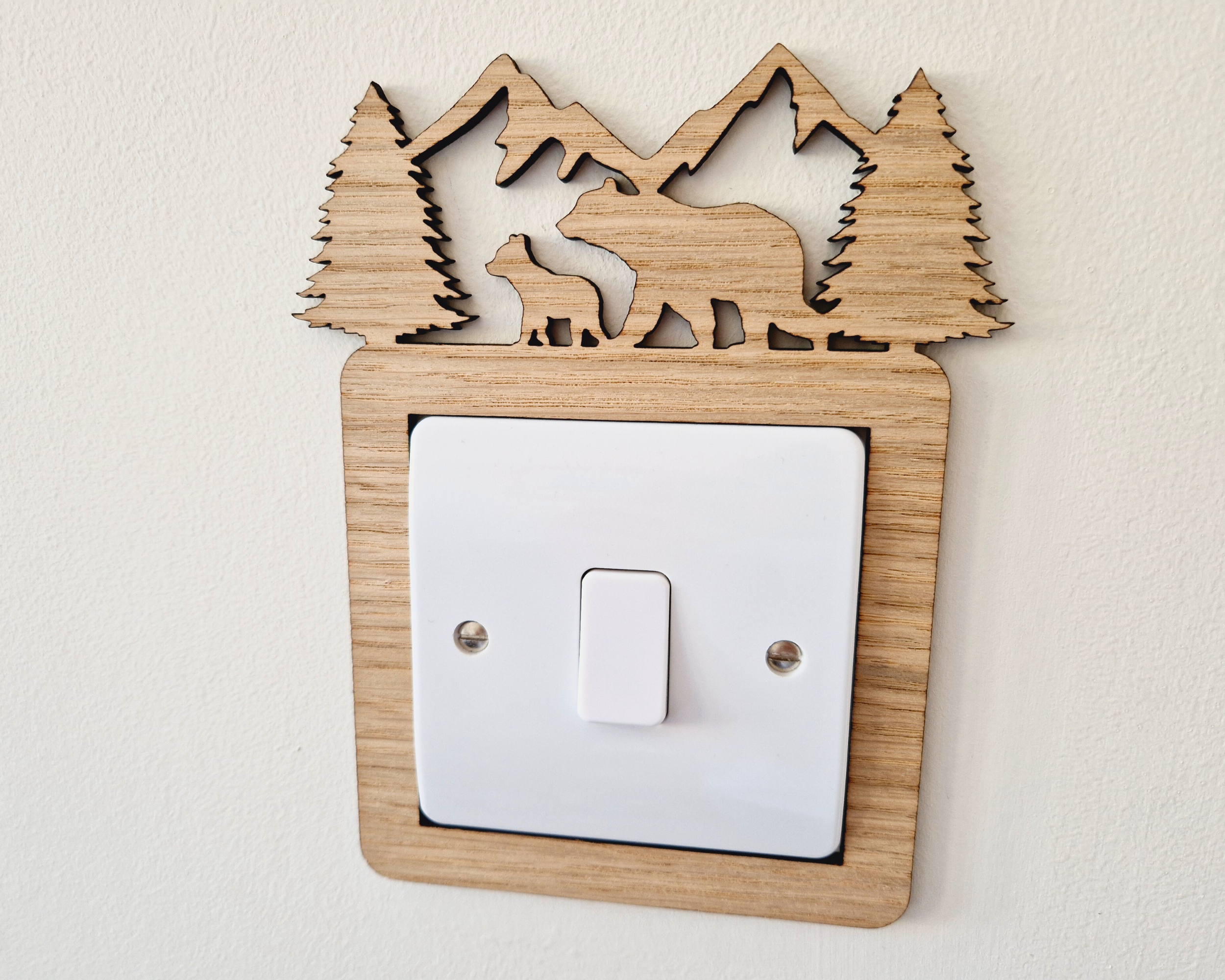 A wooden light switch with a carved design depicting a bear and pine trees on top.