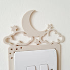 A wall-mounted light switch with a decorative crescent moon and star-shaped cutouts above it.