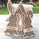 two wooden Easter bunny ornaments with names carved into them, placed on a wooden surface.
