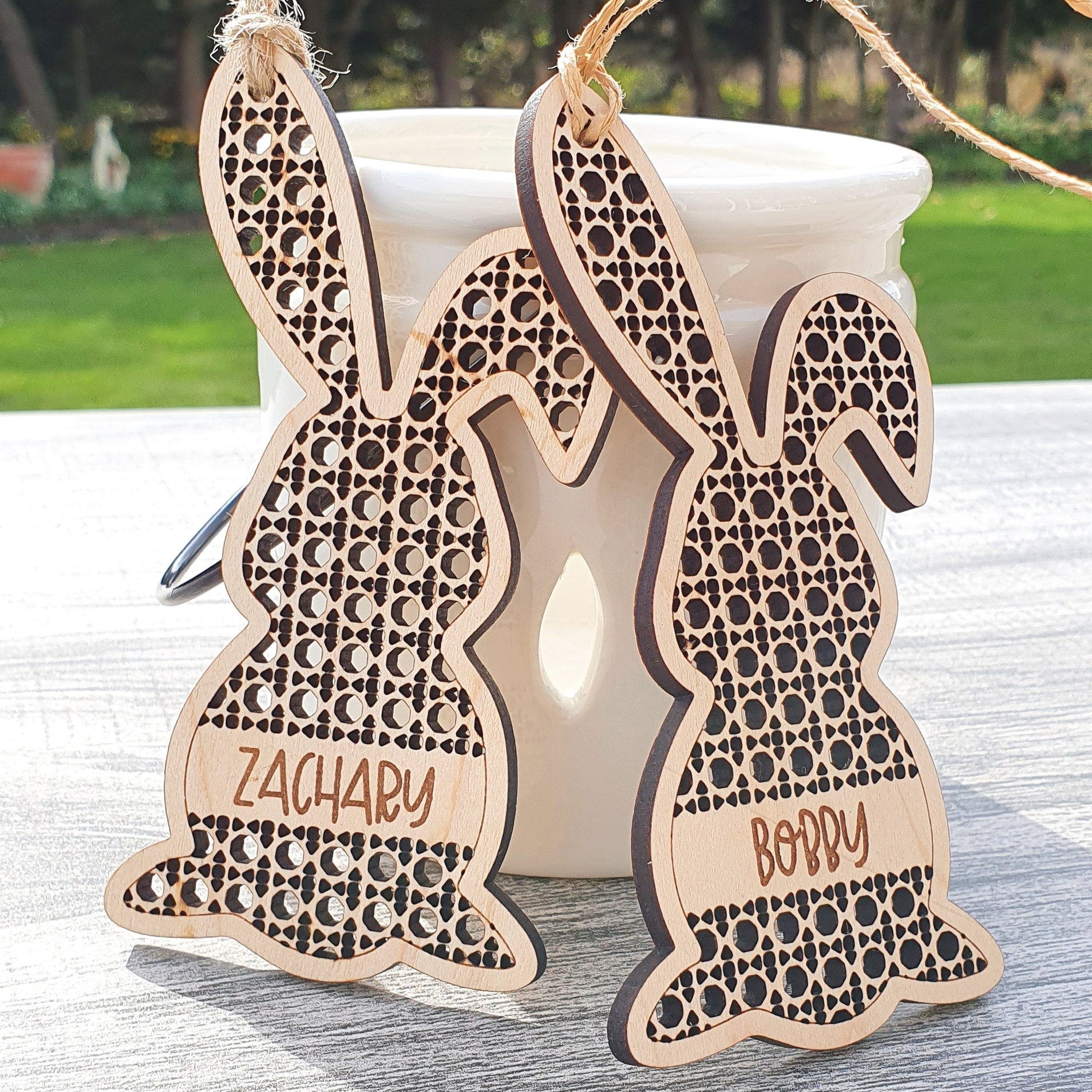 two wooden Easter bunny ornaments with names carved into them, placed on a wooden surface.