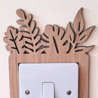 A wooden light switch with a leaf-shaped design on the top and bottom edges, mounted on a white wall.