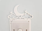 A white wall with a light switch and decorative moon and star-shaped cutouts.