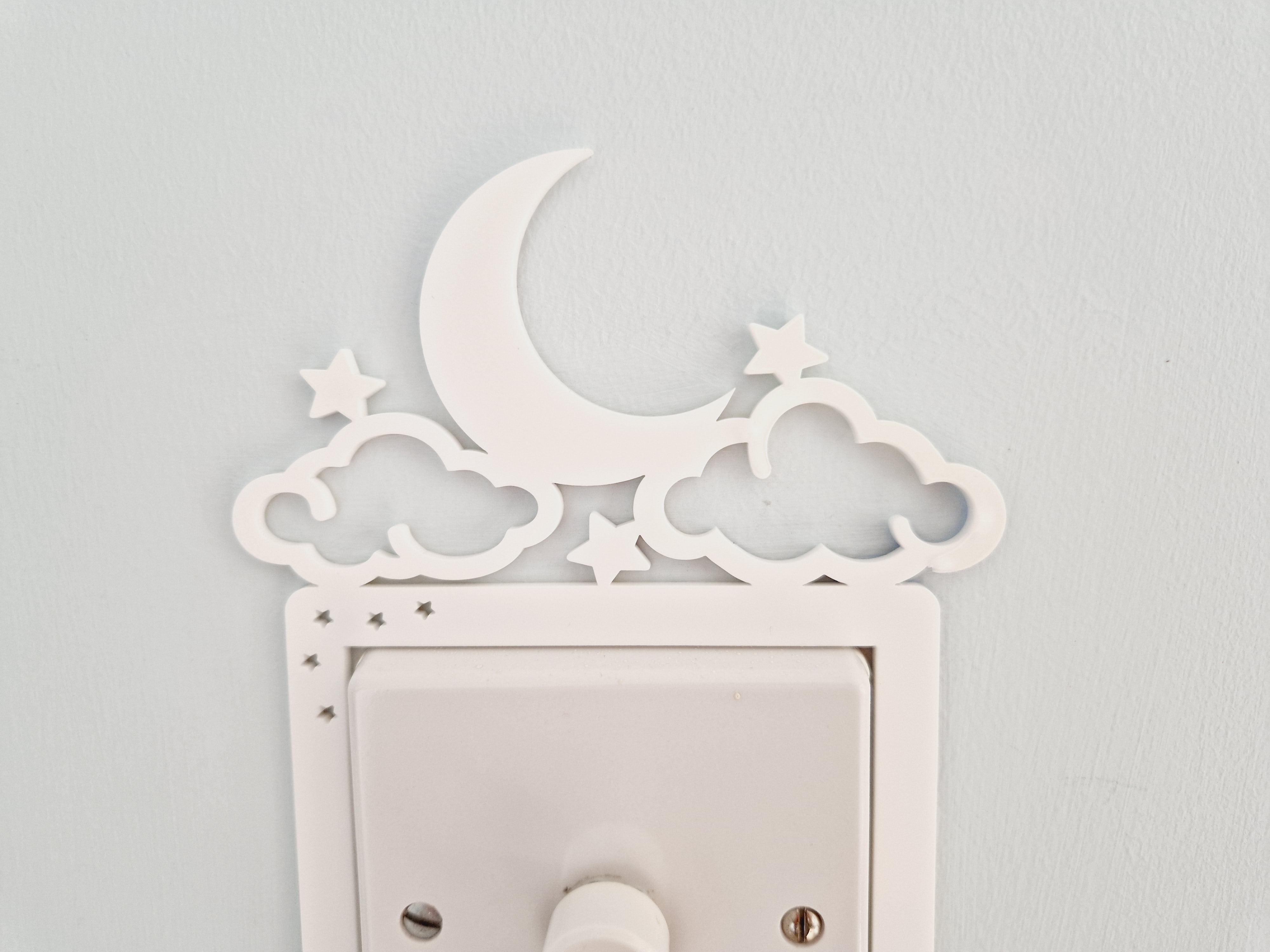 A white wall with a light switch and decorative moon and star-shaped cutouts.