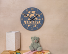 A wall clock with the name "ZACHARY" printed on it, along with a teddy bear and a children's book on a shelf.