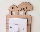 Decorative light switch cover with wooden frame and barn, tractor and tree design on a white wall.