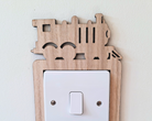 Wooden decorative switch cover with steam train cut-out designs on a white background