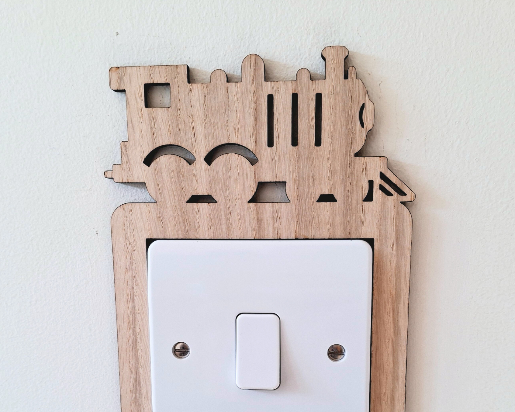 Wooden decorative switch cover with steam train cut-out designs on a white background