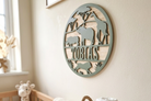 Round nursery name sign made from wood and acrylic featuring jungle animals and the name 'Tobias', above a crib, and basket of rolled up muslins.