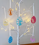 Decorative tree with colorful hanging easter themed ornaments on a white tree.