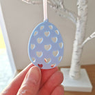 Blue decorative egg ornament with heart cutouts held by a hand against a neutral background