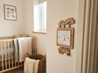 Nursery room with wooden crib, basket, and wooden decorative light switch cover with a barn, tree and tractor design.