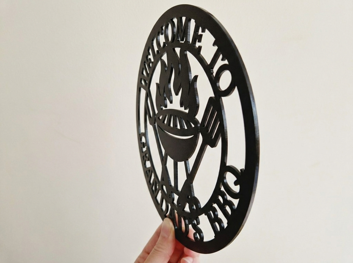 Side profile of decorative acrylic round sign with 'Welcome to the Grandad's BBQ' text and grill icon on a plain background