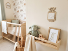 Nursery room with wooden crib, shelf with toy and picture, and a wooden light surround with highland cow and flower design. 