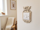 Decorative wooden light switch cover with a highland cow head and flowets on a wall with a chair and window in the background.