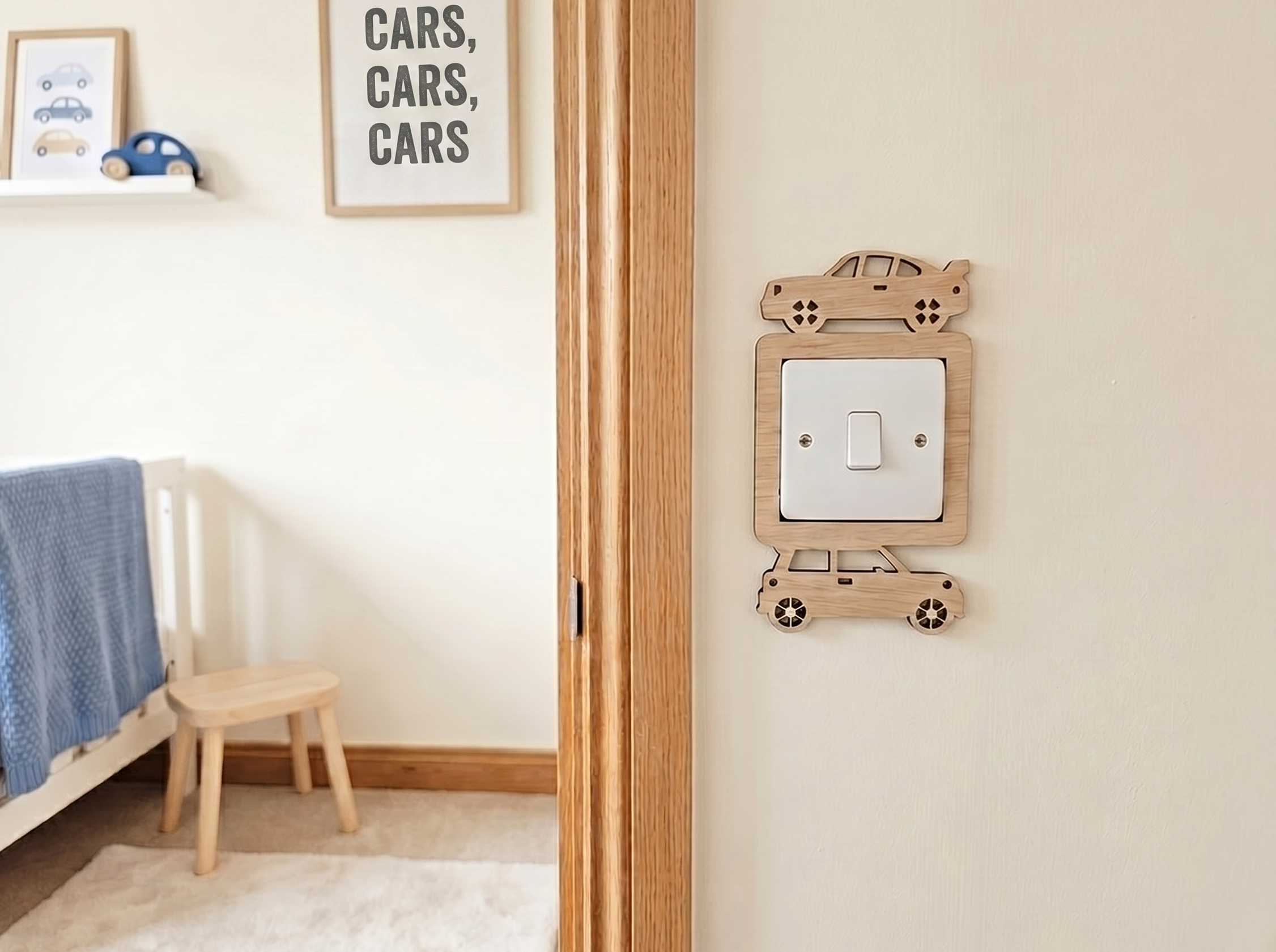 Wooden car themed light switch surround on the wall outside a children's room with a bed, chair, and wall decor featuring the word 'cars'.