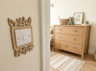 Decorative wooden switch cover with leaf design on a wall with a dresser and décor items in the background.