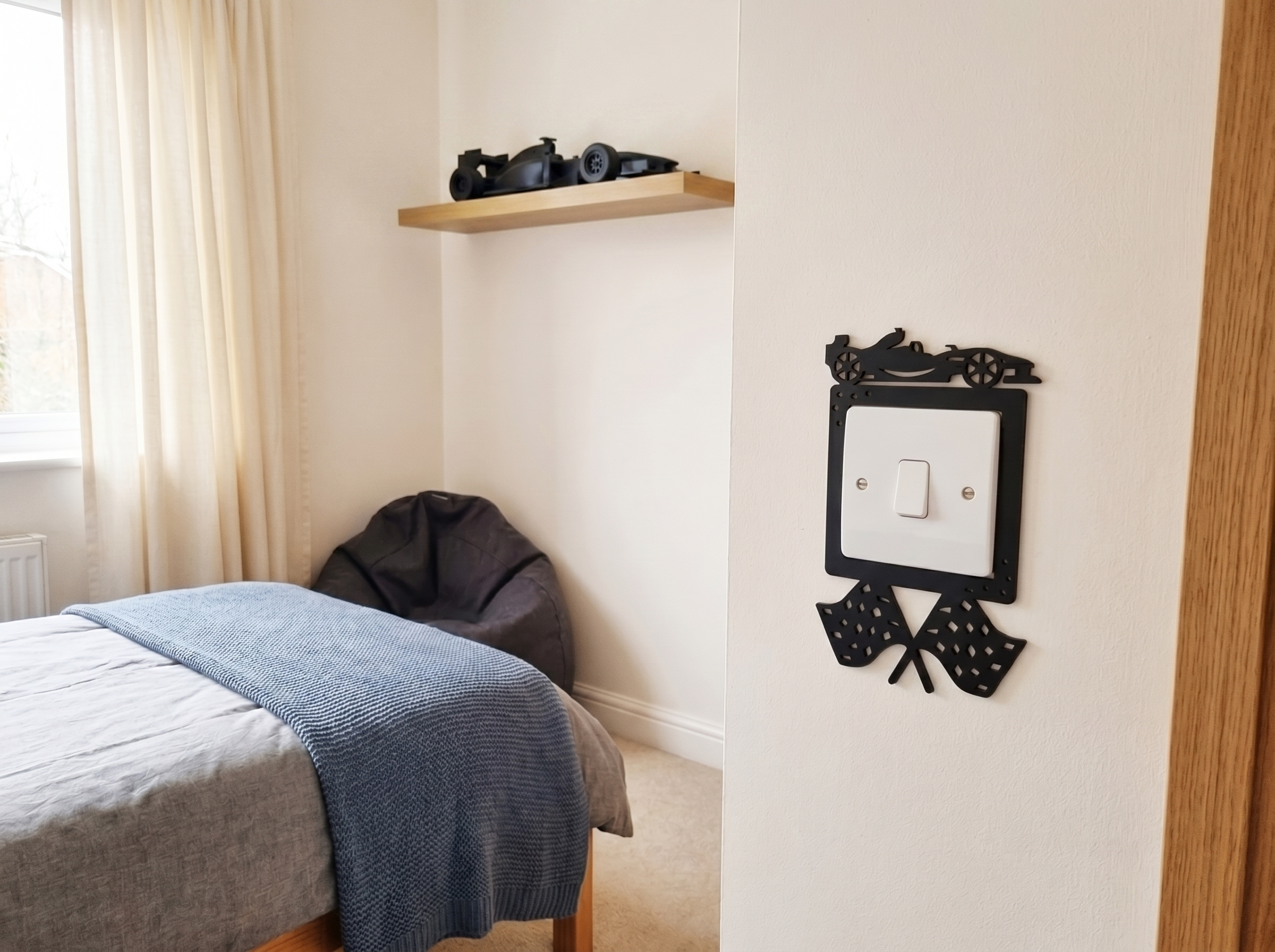 Bedroom with a bed, shelf, and decorative black racing car themed light switch cover.
