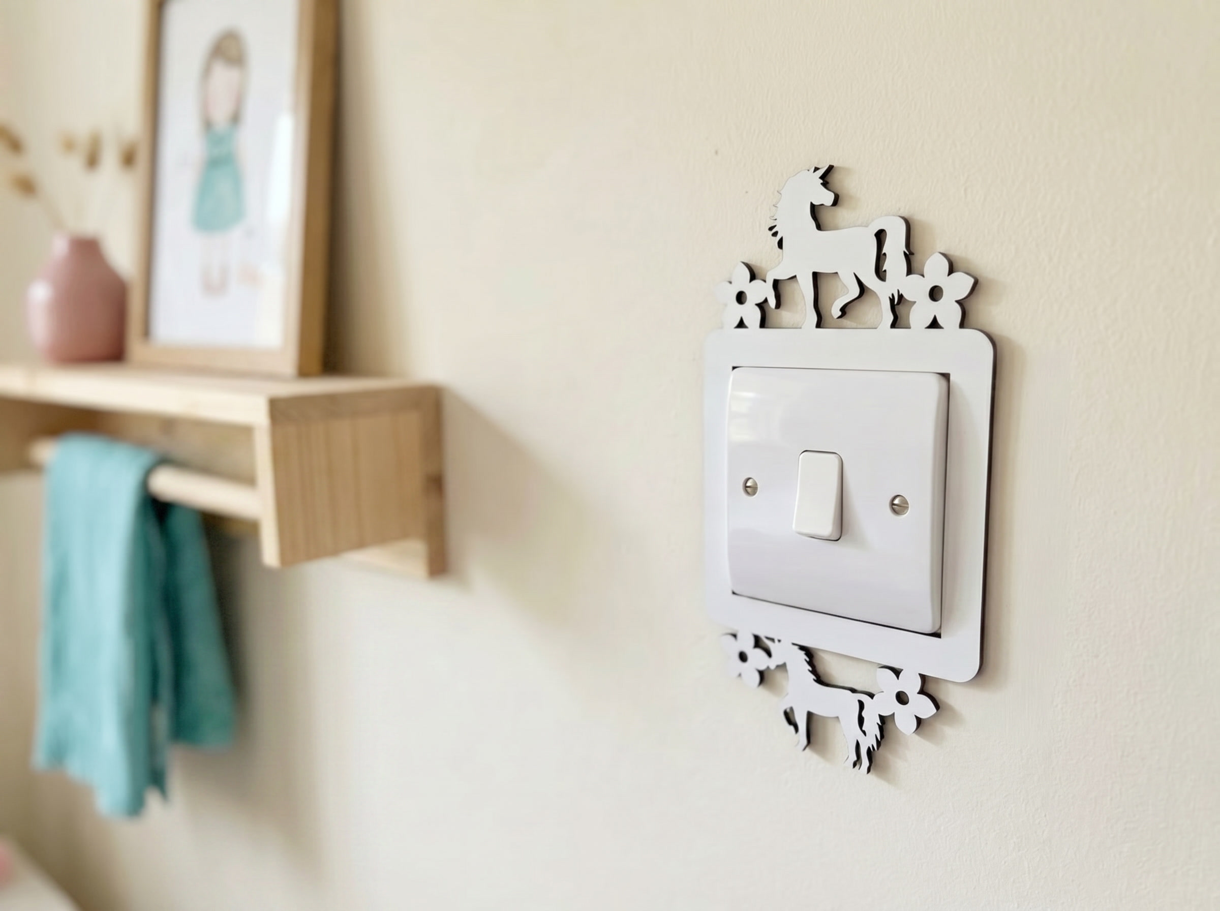 Decorative light switch cover with two unicorns and floral design on a wall next to a wooden shelf.