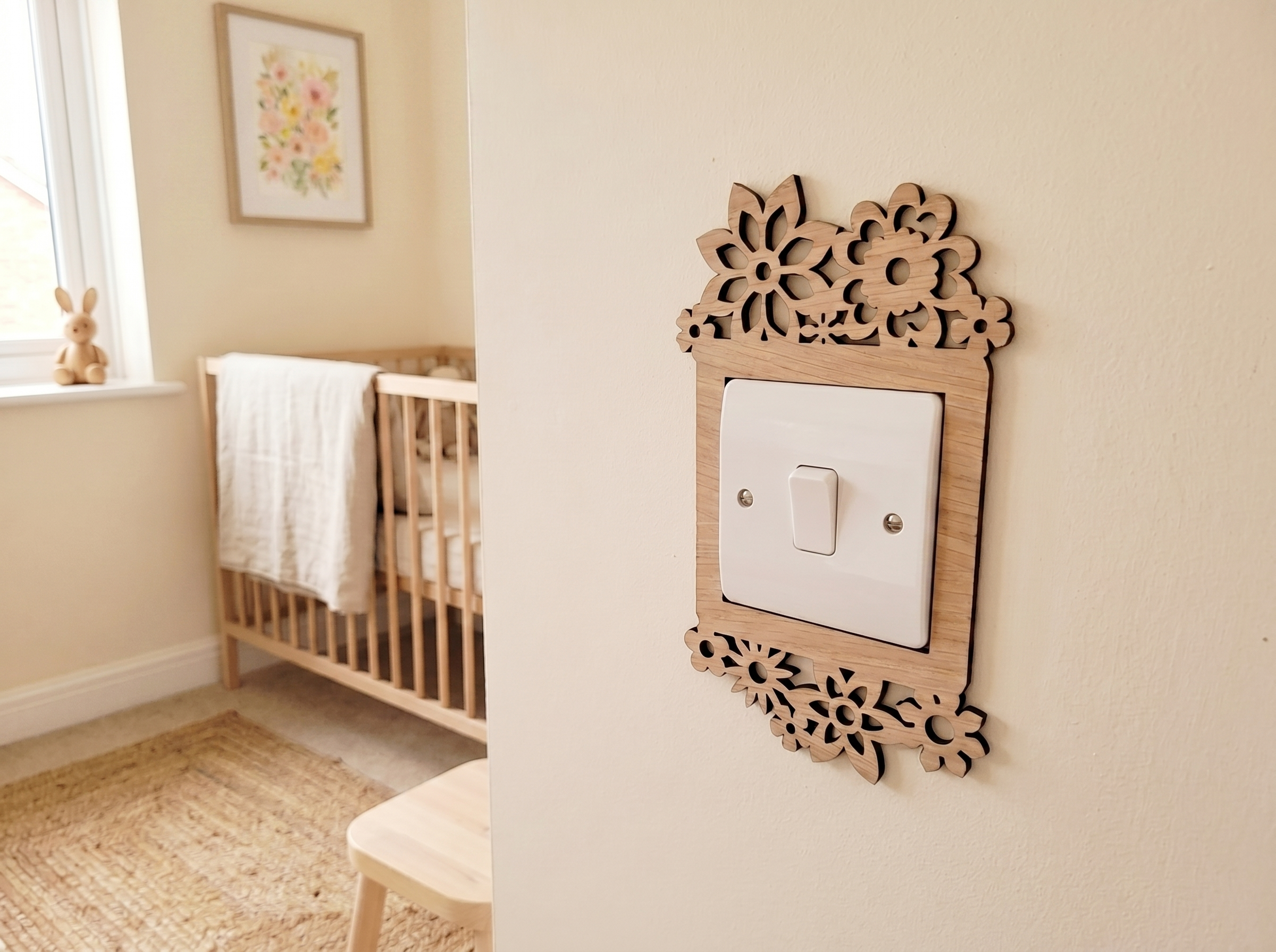 Decorative wooden light switch cover with a daisy flower design, in a nursery setting with a crib and framed picture.