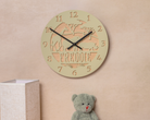 a wall clock with the name "FREDDIE" carved into it, and a small stuffed teddy bear is placed next to it on a wall.