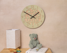 a wooden clock with the name "Olivia" carved into it, hanging on a wall above a wooden table with a teddy bear and a book.