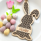 A wooden Easter bunny decoration with the name "ZACHARY" engraved on it, surrounded by colorful Easter eggs and a pink flower-shaped ornament.