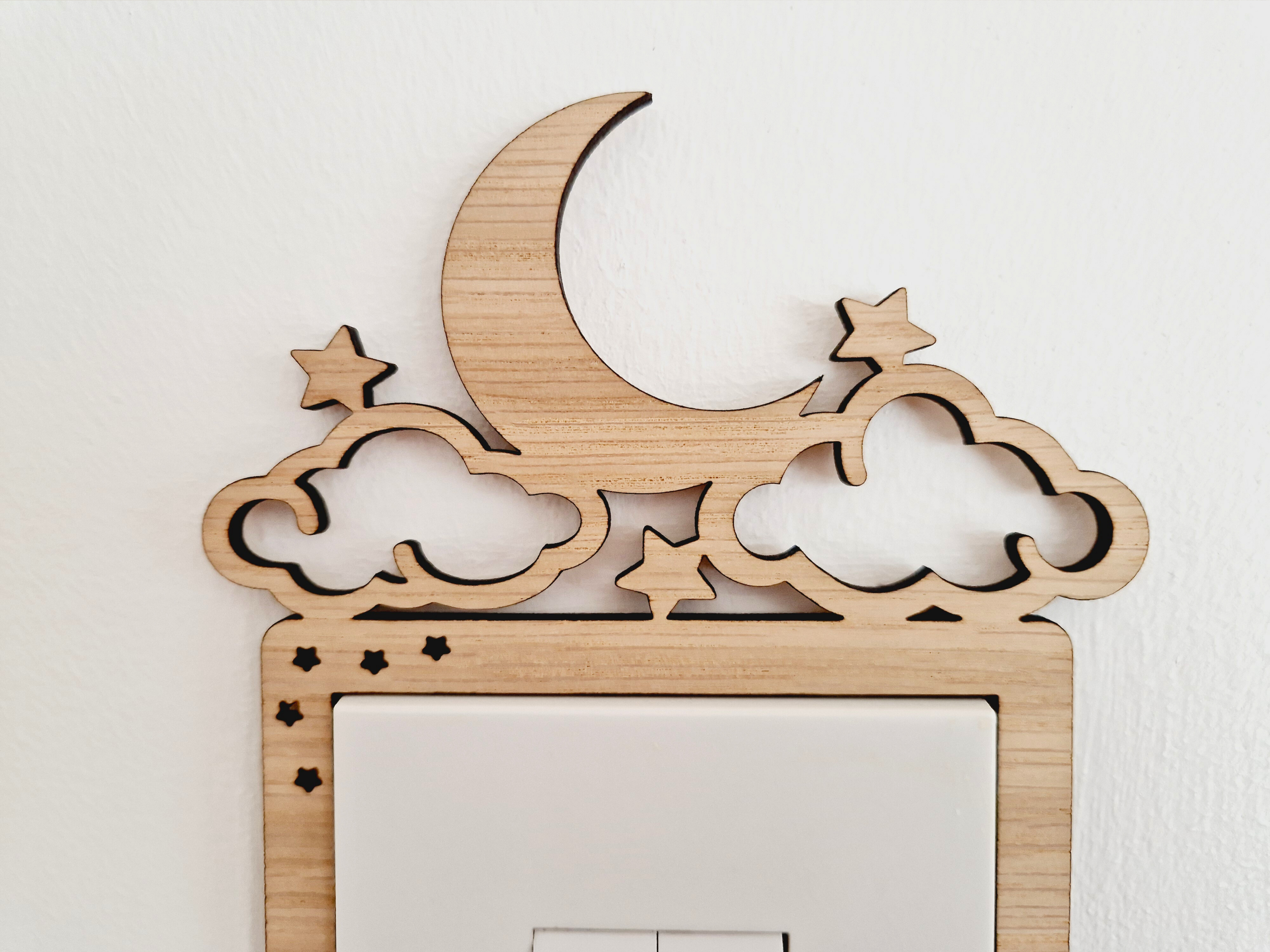 A wooden light switch with a crescent moon and stars carved into it, mounted on a wall.