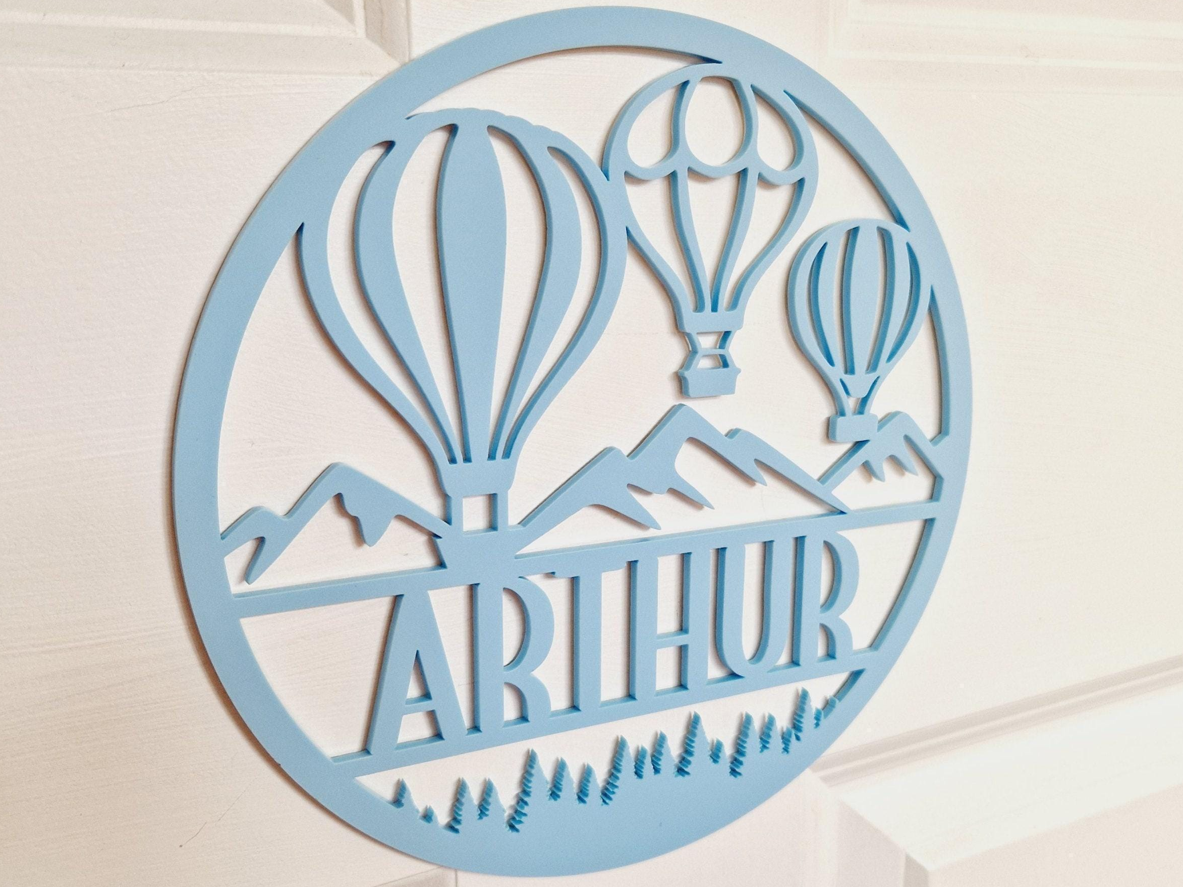 A light blue circular sign with a design featuring two hot air balloons and mountains.