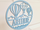A light blue circular sign with a design featuring two hot air balloons and mountains.