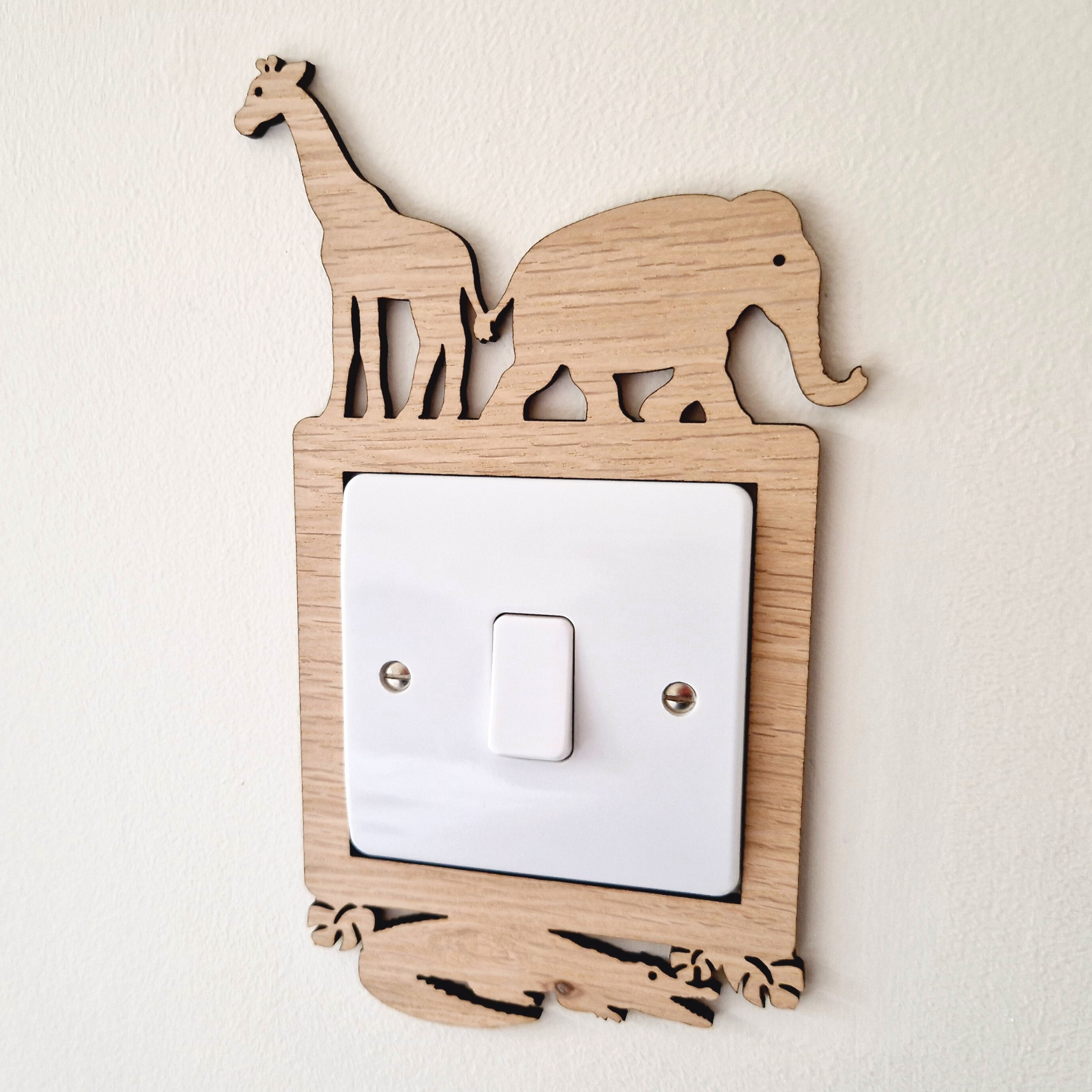 A wooden light switch with a giraffe and elephant silhouette on top, mounted on a white wall.