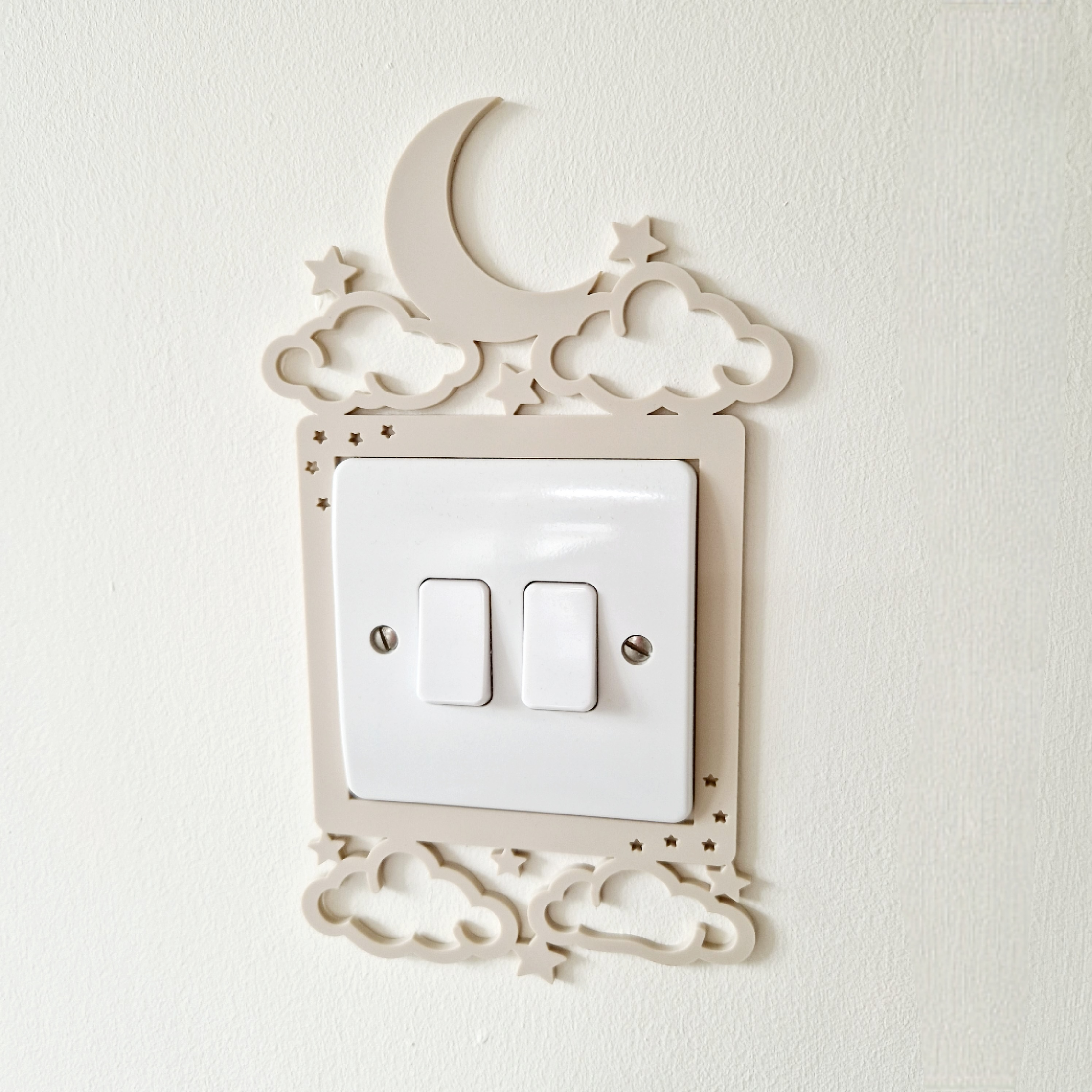 a white light switch with a decorative frame that includes a crescent moon, stars, and clouds.