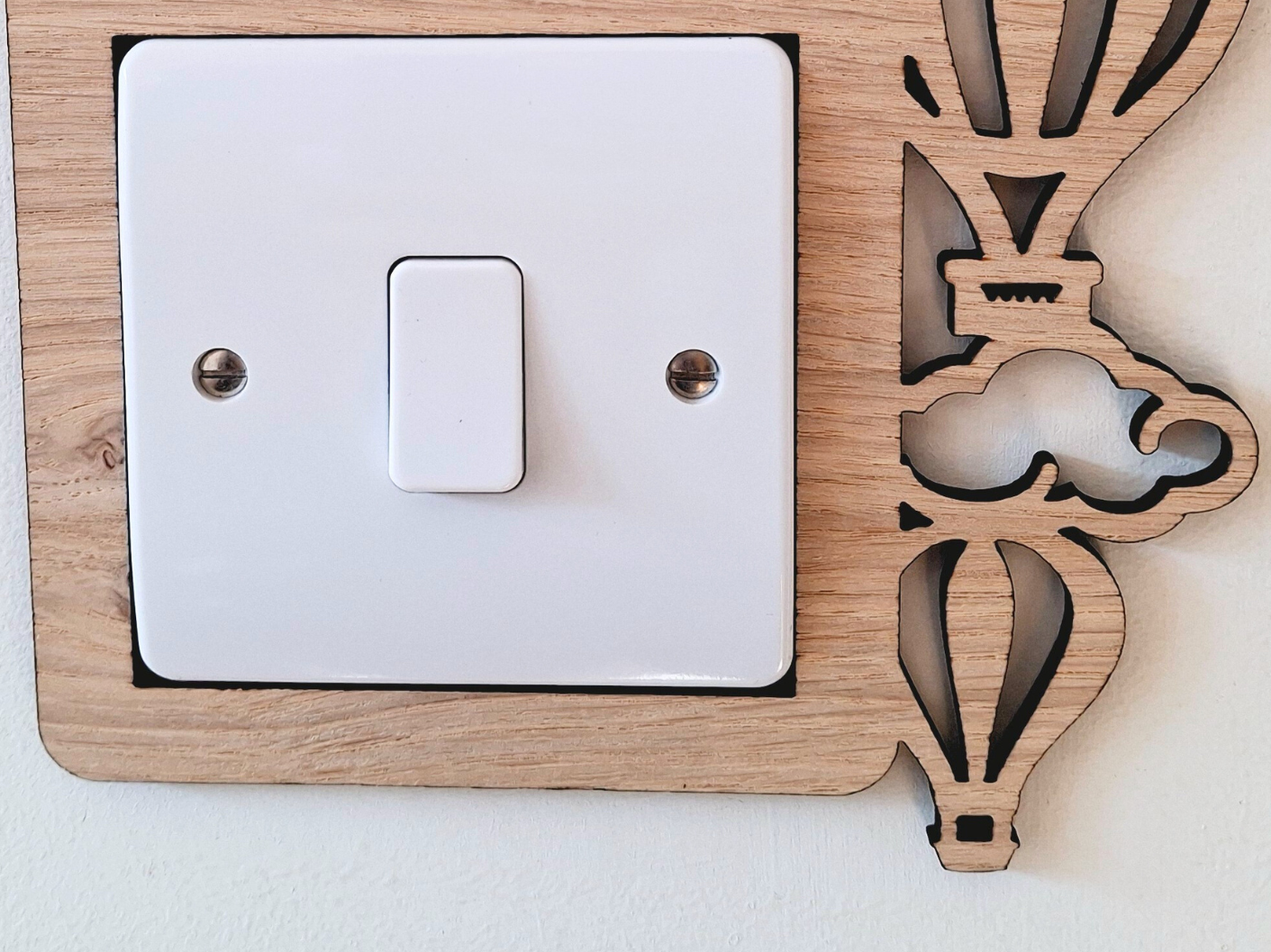 A wooden light switch with a decorative design featuring hot air balloons and clouds.