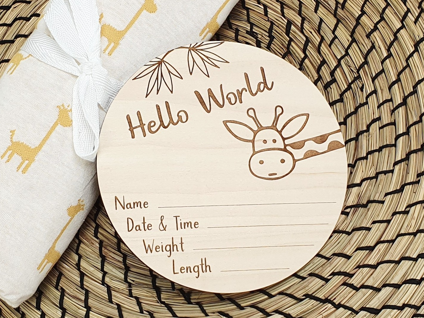A wooden baby name card with a giraffe design, placed on a woven placemat.