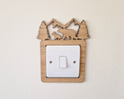 A wooden light switch with a carved design depicting a bear and pine trees on top.