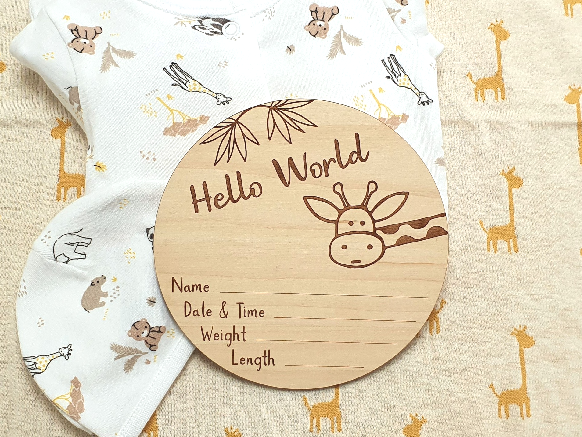 A wooden baby name card with a giraffe design, placed on a beige fabric with a giraffe pattern.