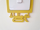 A yellow plastic construction vehicle-shaped light switch cover is attached to a white wall.