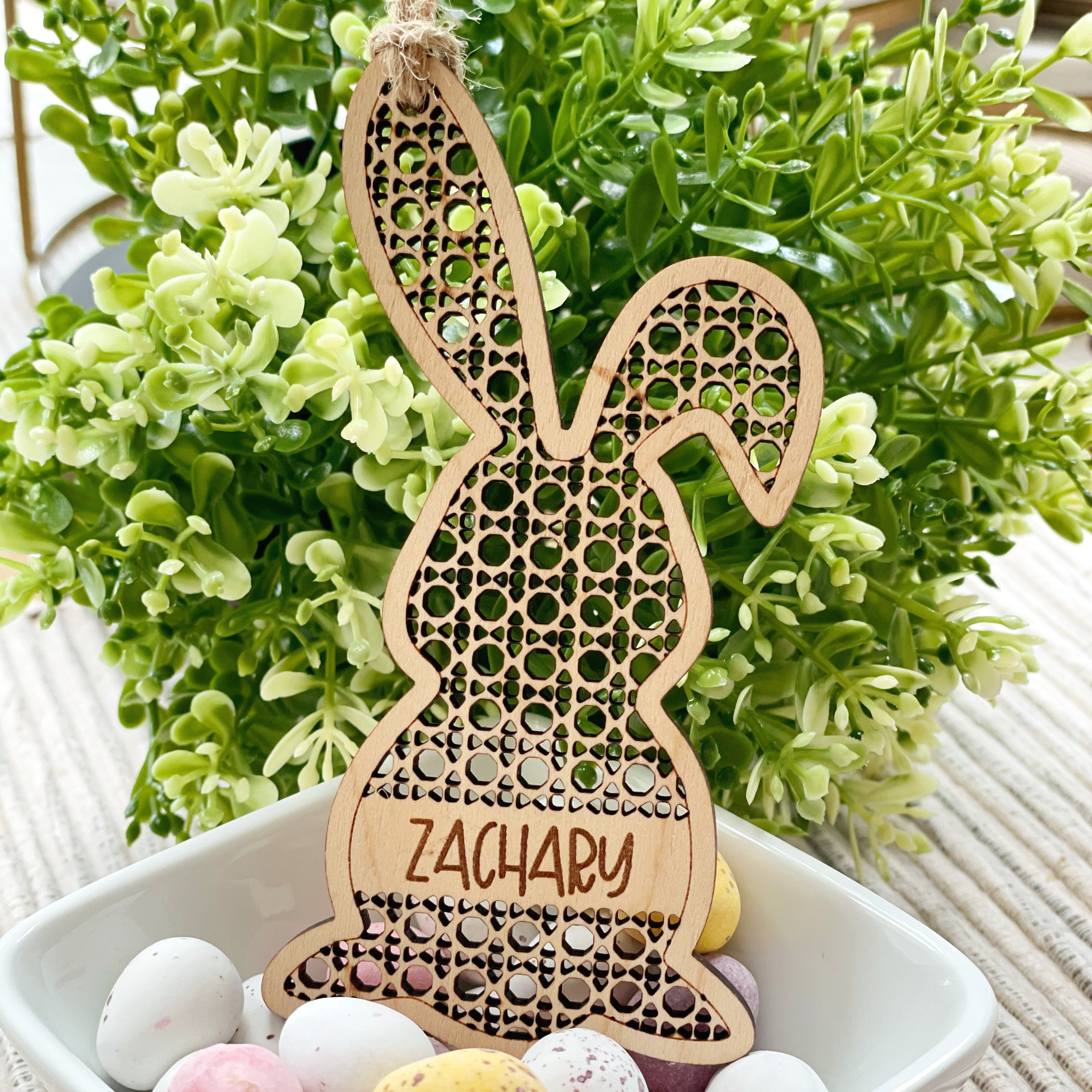 A wooden Easter bunny decoration with the name "ZACHARY" engraved on it, placed in a bowl filled with colorful Easter eggs.