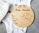 A wooden baby name card with a picture of an elephant and the text "Hello World" is placed on a white cloth.